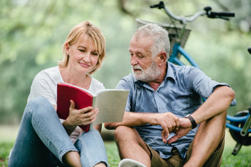 Happy elderly couple with smiling face enjoying together, reading a book in the park, spending time and relaxing time concept.