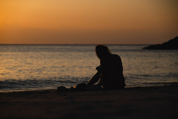 Young asian lady sits in front of a beach during sunset in Koh Lanta (Krabi, Thailand)