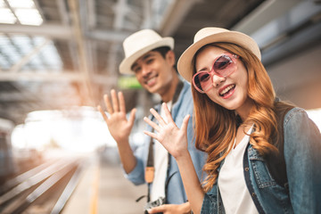 Happy Asian couple traveler holding a mobile phone in station and waiting for train in vacation time.Two Asian Tourists With Backpacks Train travel in Sightseeing City Thailand.