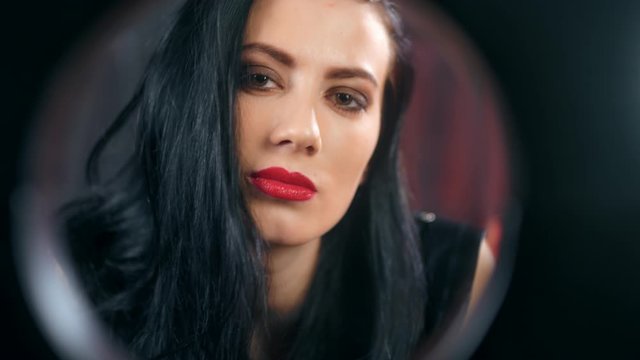 Face of sensual domination female in latex contemplating from black circle frame feeling passion