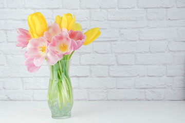 close up of colorful tulips floral arrangement in a clear vase with a white brick background