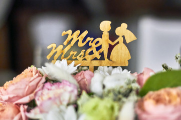 Wooden figurines of the bride and groom in the frame of wedding flowers