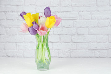 close up of colorful tulips floral arrangement in a clear vase with a white brick background