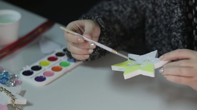 A young woman makes home decorations for Christmas by painting stars with watercolors