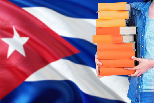 Cuba national education concept. Close up of female student holding colorful books with country flag background.