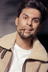 A man in a white sheepskin coat under a sheepskin holds a cigarette in his mouth and wants to laugh