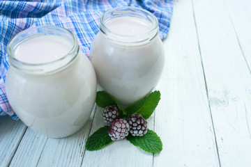 Blackberry yogurt in jars on a white wooden background.