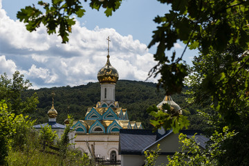 Fototapeta na wymiar Church with a golden dome against the backdrop of mountains and clouds, in the foreground oak leaves