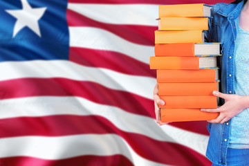 Liberia national education concept. Close up of female student holding colorful books with country flag background.