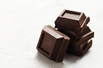 Broken dark chocolate pieces on a light background. View from above. Top view.