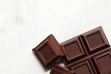 Broken dark chocolate pieces on a light background. View from above. Top view.