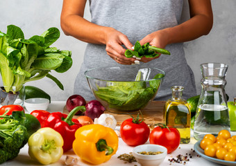 Woman is preparing green salad of romaine lettuce, cooking salad in a glass bowl in the kitchen. Healthy diet concept.