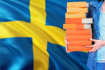 Sweden national education concept. Close up of female student holding colorful books with country flag background.