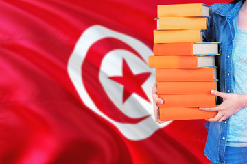 Tunisia national education concept. Close up of female student holding colorful books with country flag background.