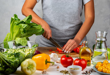 Woman cuts red pepper and makes salad in the kitchen. Healthy diet concept.