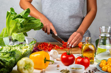 Woman cuts red pepper and makes salad in the kitchen. Healthy diet concept.