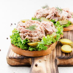 Homemade tuna salad sandwiches on cutting board with pickles aside