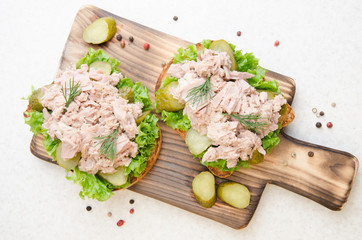 Flat lay view at homemade tuna salad sandwiches on cutting board with pickles aside