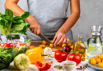 Woman cuts yellow cherry tomatoes and cooking salad in the kitchen. Healthy diet concept.