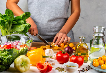 Woman cuts yellow cherry tomatoes and cooking salad in the kitchen. Healthy diet concept.