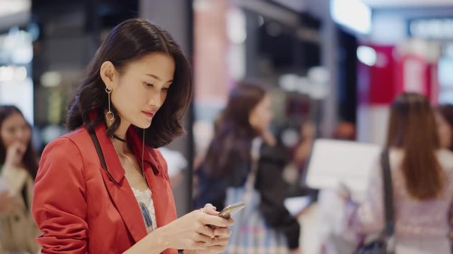 Attractive Asian woman in a shopping mall uses her futuristic smartphone to project a holographic grid map into the air above her device