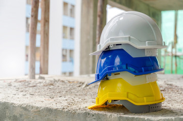 white, blue and yellow hard safety helmet for safety accident stack on floor at workplace in...