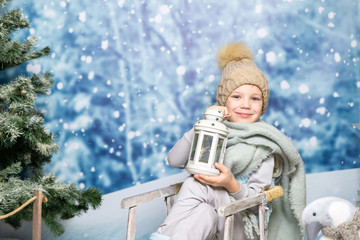 a little boy in winter clothes with a lantern sitting on a sleigh