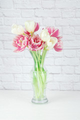Pink and white tulips arranged in a clear vase isolated on a white brick background