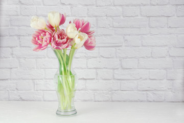 Pink and white tulips arranged in a clear vase isolated on a white brick background
