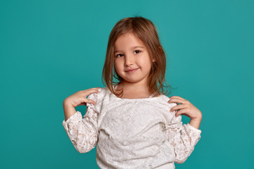 Little girl in a white sweater on a blue background. Emotions of a child. Close-up studio shot of a beautiful little girl.