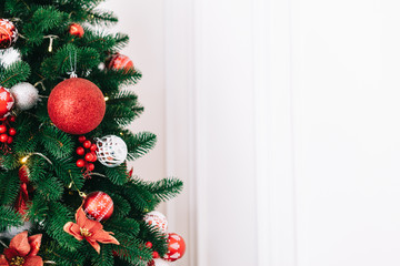 A fragment of a Christmas tree decorated with red balls on a white wall background