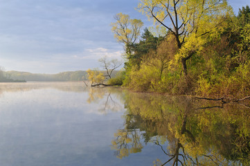 Spring shoreline of Whitford Lake at sunrise with reflections in calm water, Fort Custer Recreation Area, Michigan, USA