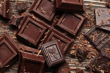 Dark chocolate pieces and bar on a brown table. Top view. Place for text.