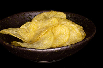 Lot of whole crisp potato chip in glazed bowl isolated on black glass