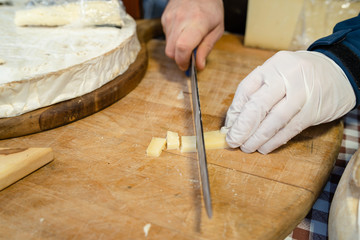 Close up on midsection hands of the man sale selling the french cheese saint nectaire holding big knife on the board at his store cutting cut in the pieces