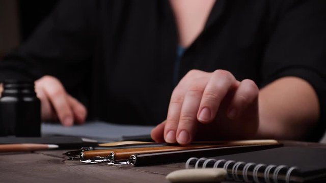 View of hand taking stylus, dipping in ink and writing or drawing on the paper. Fine penmanship. Words are not visible for the viewer. Sliding focus. 4k.