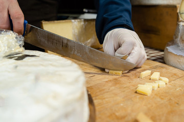 Close up on midsection hands of the man sale selling the french cheese saint nectaire holding big knife on the board at his store cutting cut in the pieces