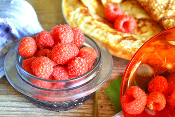 fresh raspberries in travsparent bowl with golden russian thin pancakes on shabby table