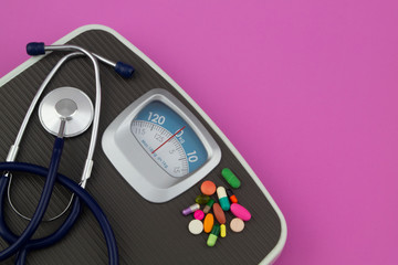 Scale, stethoscope and drugs on pink background with copyspace for text. Loose weight and healthcare concept.