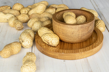 Lot of whole tasty beige peanut in bamboo bowl on round bamboo coaster on white wood