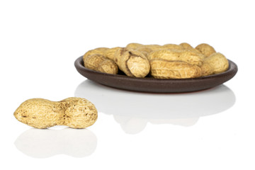 Lot of whole tasty beige peanut one in focus with brown ceramic coaster isolated on white background
