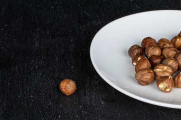 Lot of whole tasty brown hazelnut on white ceramic plate on grey stone