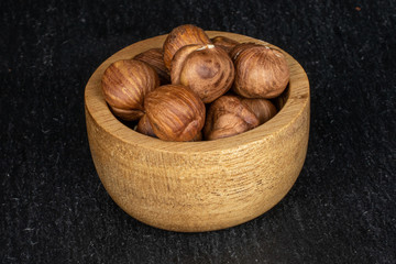 Lot of whole tasty brown hazelnut in bamboo bowl on grey stone
