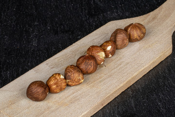 Group of eight whole tasty brown hazelnut on wooden cutting board on grey stone