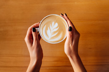 Female hands with cup of hot tasty coffee in cafe, close up view