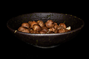 Lot of whole tasty brown hazelnut in glazed bowl isolated on black glass