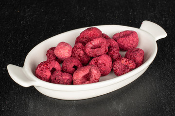 Lot of whole dried raspberry on white ceramic plate on grey stone