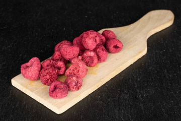 Lot of whole dried raspberry on wooden cutting board on grey stone
