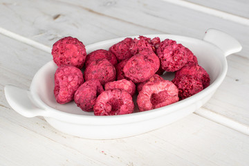 Lot of whole dried raspberry on white ceramic plate on white wood