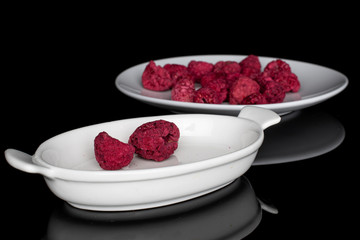 Lot of whole bright dried raspberry on white ceramic plate isolated on black glass